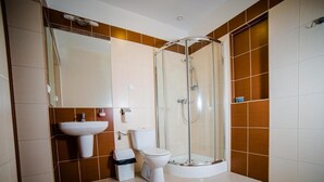Un baño con ducha envuelta en vidrio, un lavamanos y un inodoro.