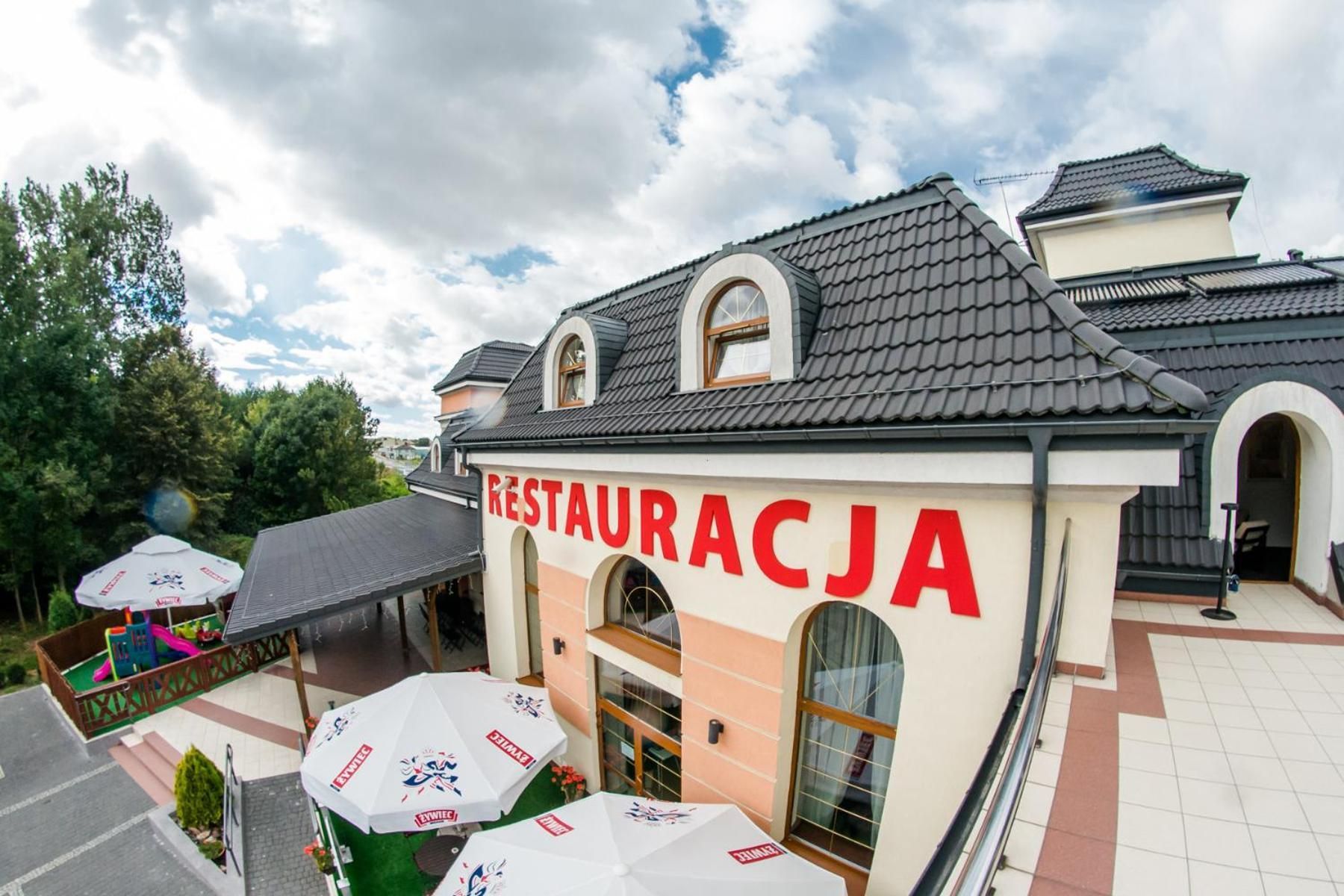 Een restaurant met een betegeld dak en een bord waarop 'RESTAURACJA' staat. Er zijn buiten parasols met logo's.