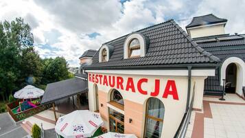 A restaurant with a tiled roof and a sign reading 'RESTAURACJA'. There are outdoor umbrellas with logos.