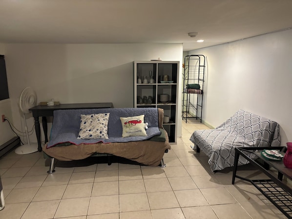 A living room with a sofa, a table, a fan, and a shelving unit.
