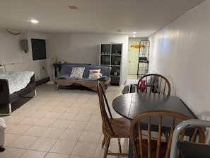A compact living space with a dining table, chairs, a sofa, and a shelving unit.