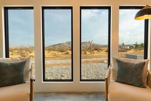 A room with a large window, a sofa, and a lamp. - Hōkū Hale | Spa | Sauna | Fire Pit | 360° Views (Joshua Tree)