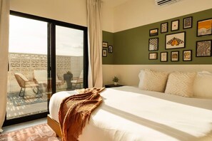 Une chambre d’hôtel avec un lit, une vue à travers une porte coulissante, un mur orné de tableaux encadrés et une chaise près de la porte.