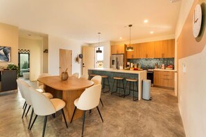A modern kitchen with a central island, bar stools, and a dining area with a round table and chairs. - Hōkū Hale | Spa | Sauna | Fire Pit | 360° Views (Joshua Tree)