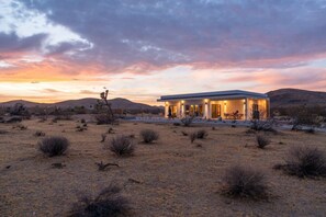 A modern house with a flat roof, large windows, and a patio area. - Hōkū Hale | Spa | Sauna | Fire Pit | 360° Views (Joshua Tree)