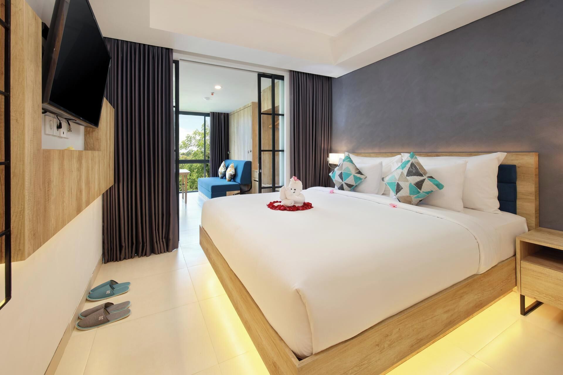Une chambre d’hôtel moderne dotée d’un grand lit, d’un téléviseur fixé au mur et offrant une vue sur l’extérieur grâce à une porte coulissante.
