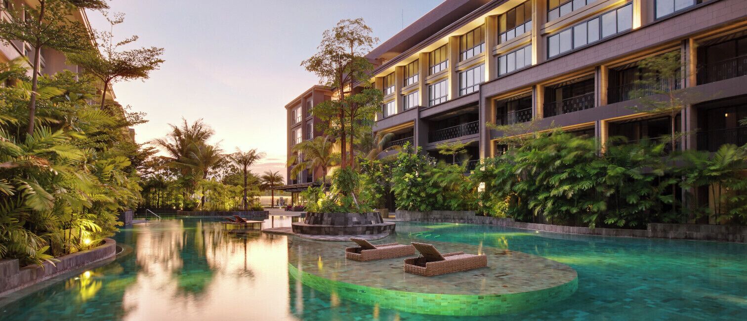 A hotel with a pool area, lounge chairs, and lush greenery.