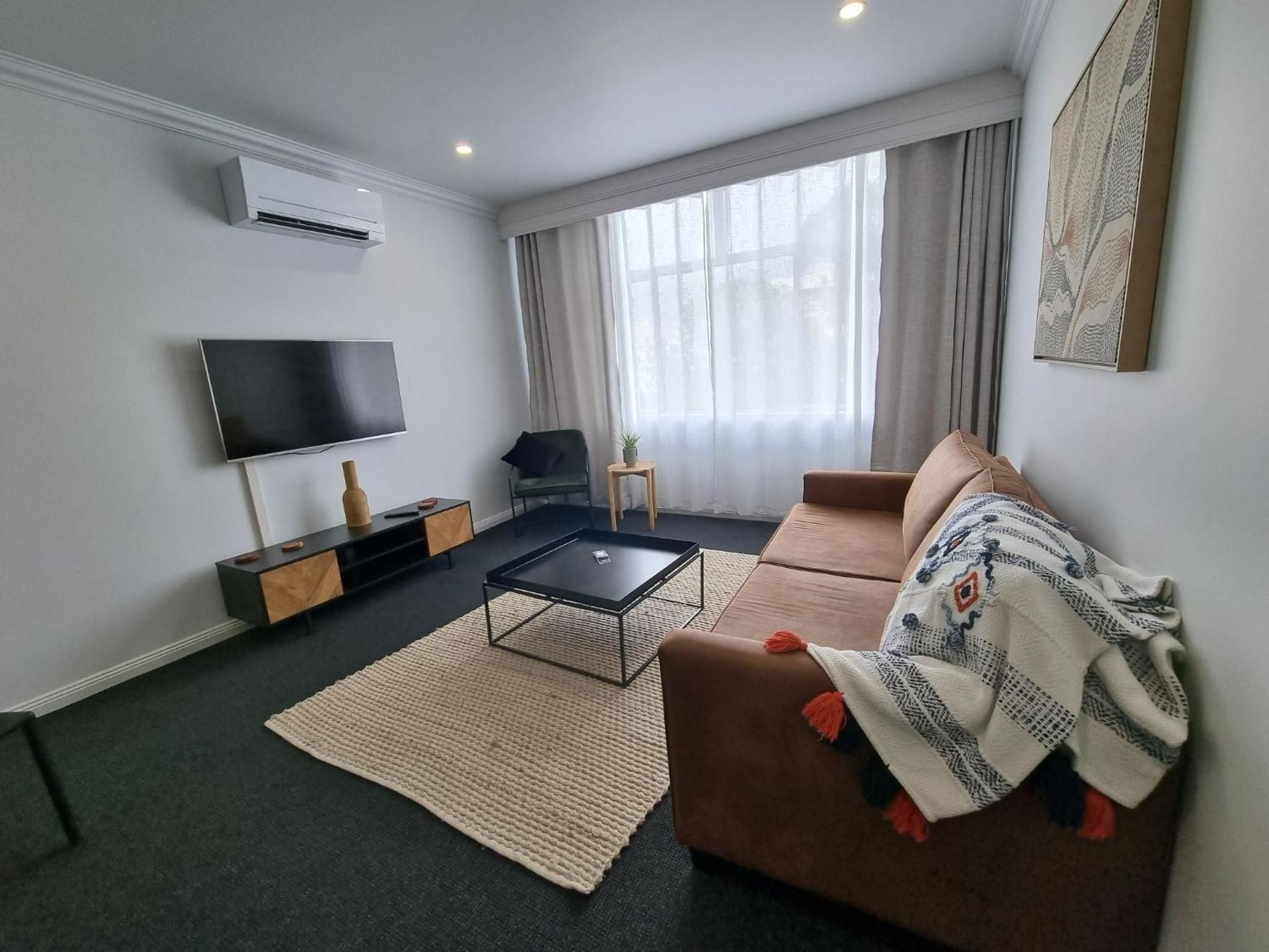 A modern living room with a flat-screen TV, a sofa, a coffee table, and a large window with curtains.