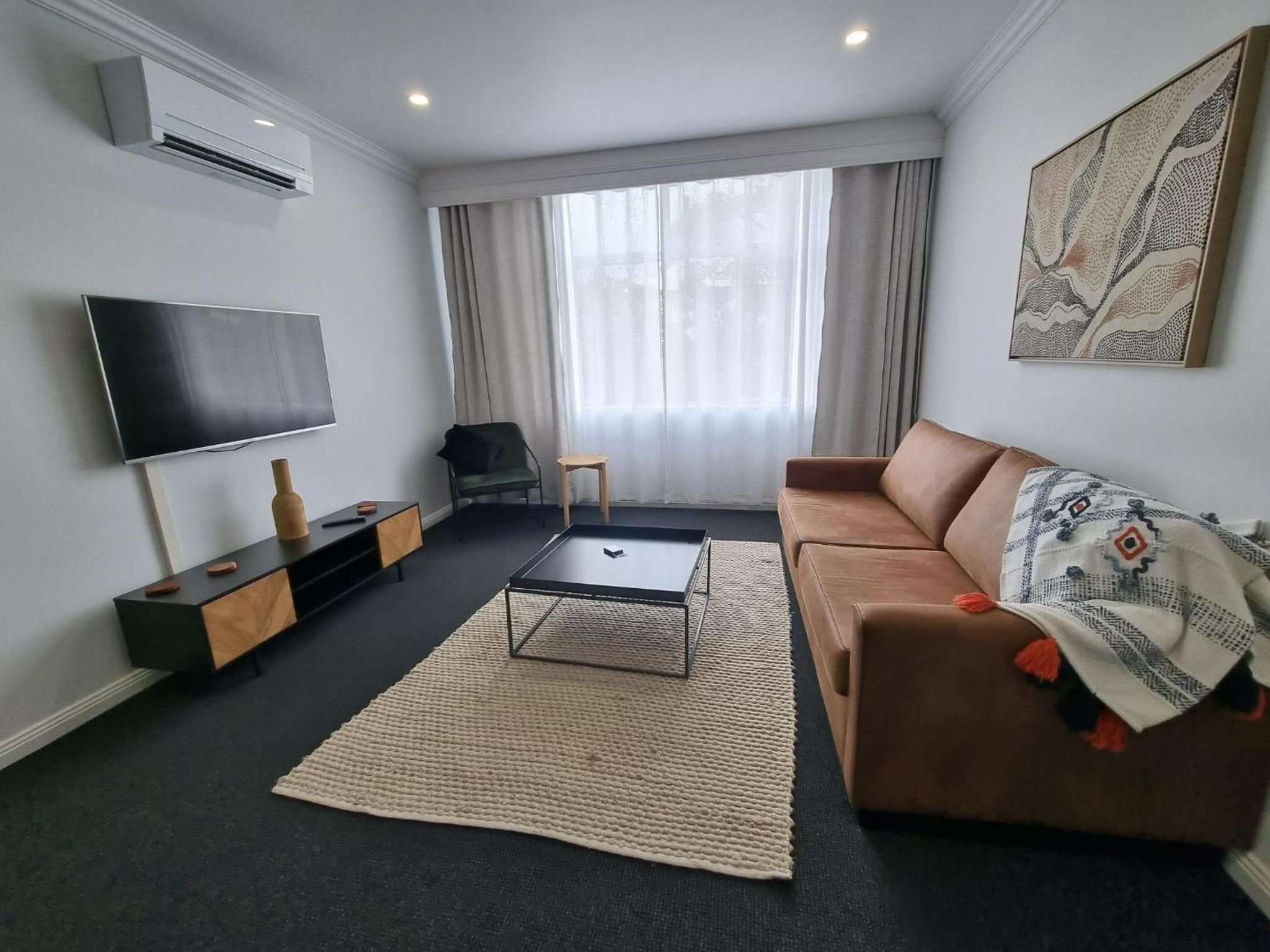 A modern living room with a flat-screen TV, a brown sofa, a coffee table, and a large window with curtains.