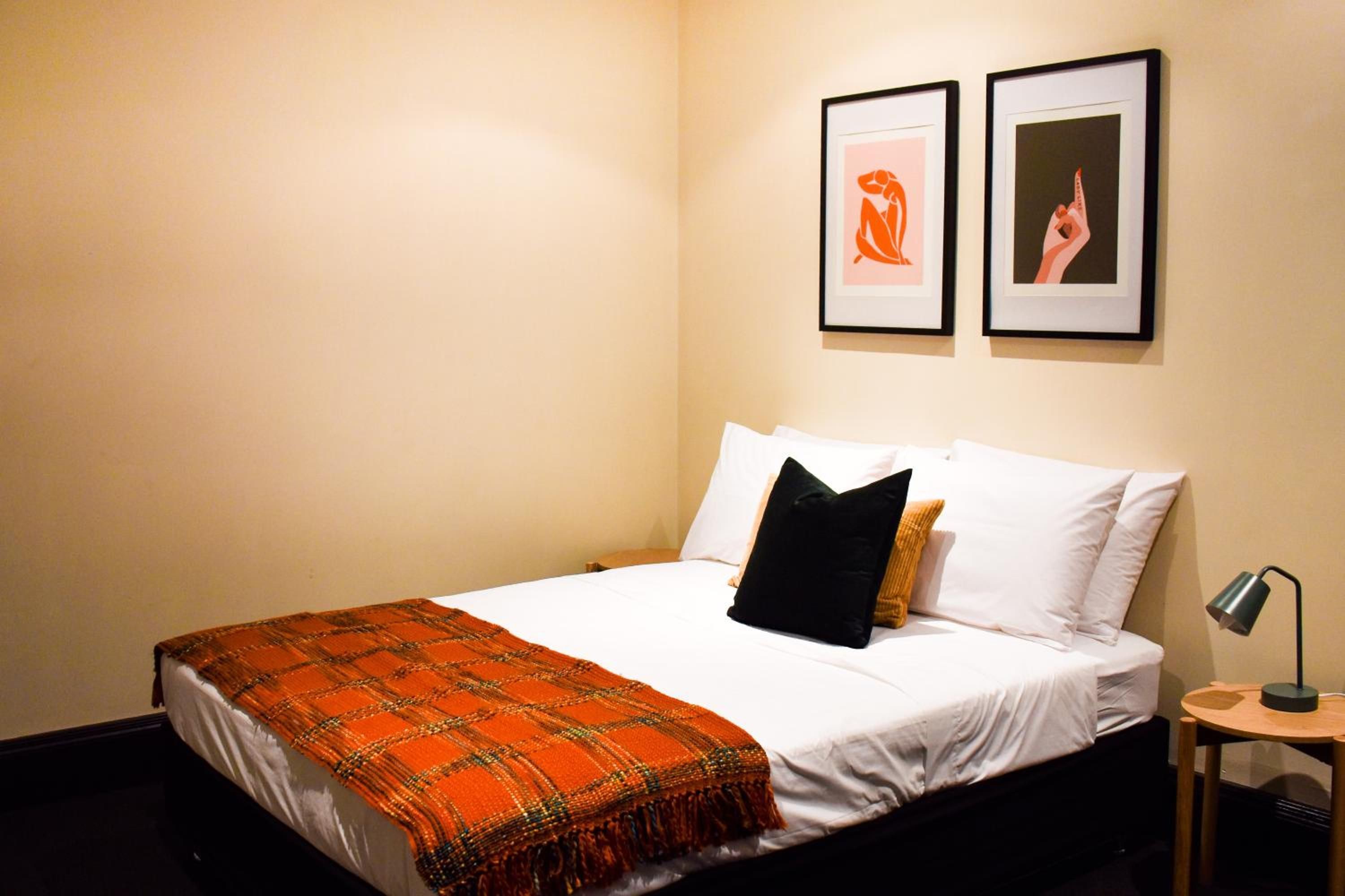 A hotel room with a bed, a nightstand, a lamp, and two framed pictures on the wall.