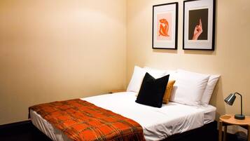 A hotel room with a bed, a nightstand, a lamp, and two framed pictures on the wall.