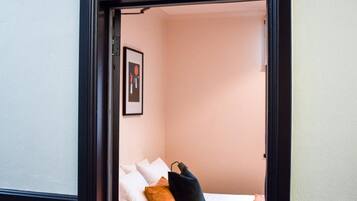 A narrow doorway leading to a small room with a bed, a framed picture on the wall, and a decorative stained glass window above the door.