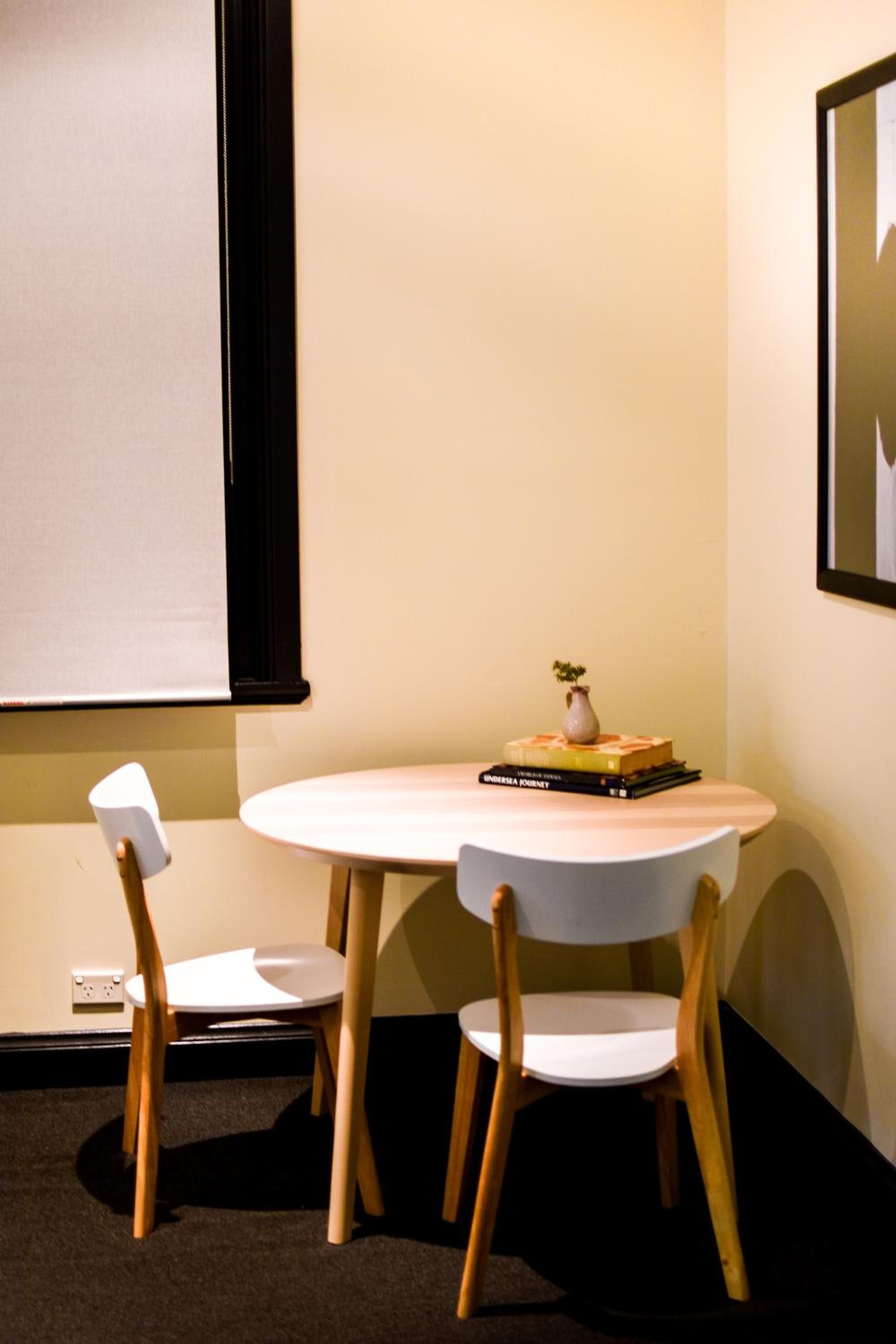 A small, round table with two chairs, a vase with a plant, and a stack of books.