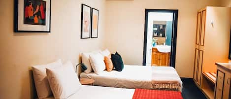 Une chambre d’hôtel avec deux lits, un plaid rouge, une petite table ronde et une armoire.