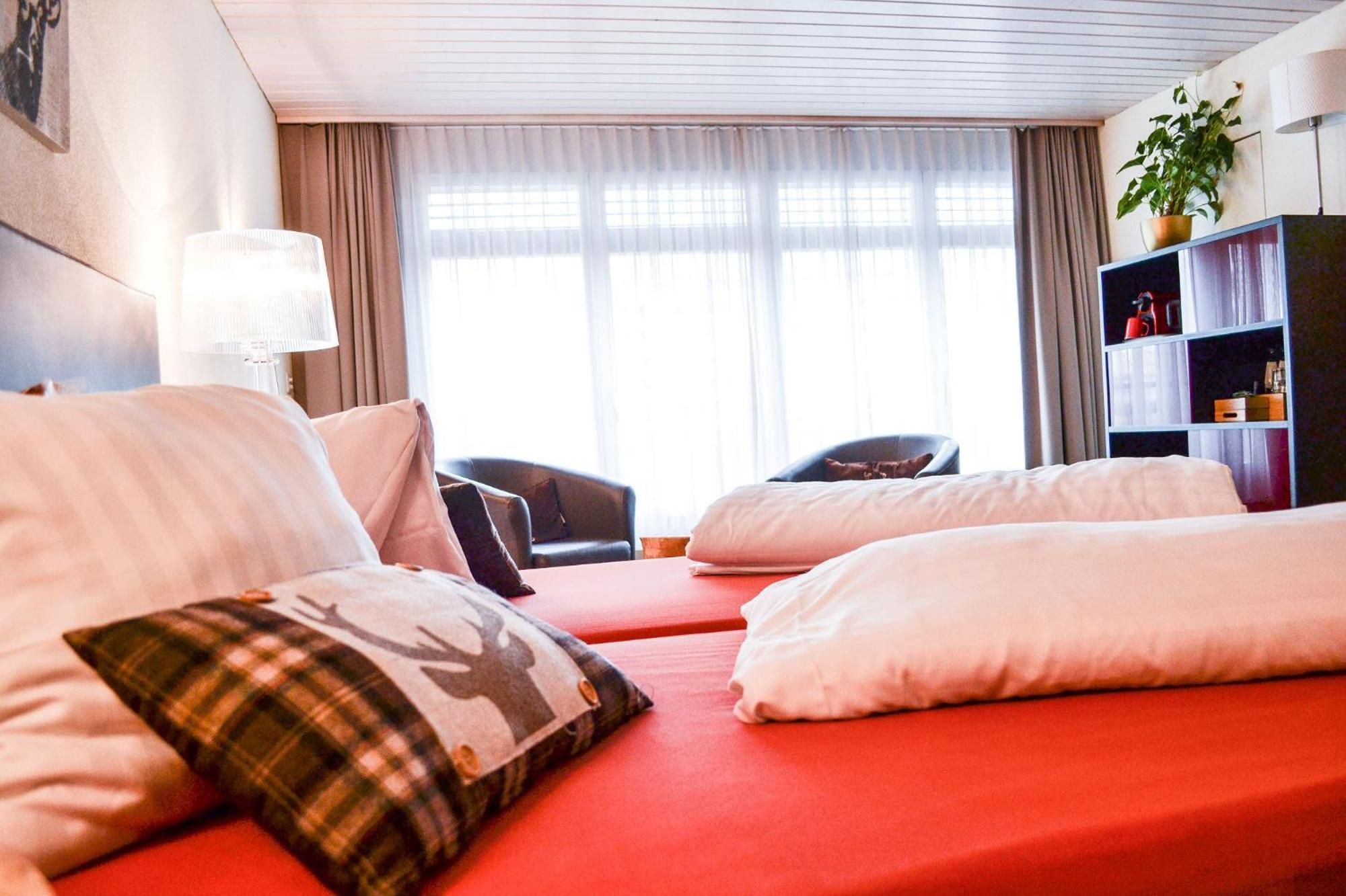 A hotel room with two beds, a desk, a chair, a bookshelf, and a window with curtains.