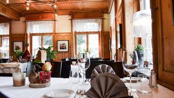 A dining area with wooden ceiling beams, large windows, and a table set for a meal.