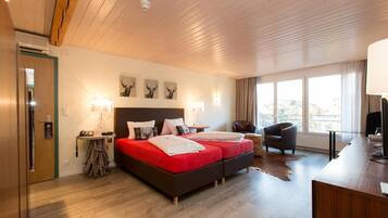 A hotel room with a wooden ceiling, a bed with red bedding, a desk with a computer, and a chair.
