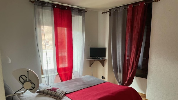 Un dormitorio con cama, televisor sobre un mueble y cortinas.