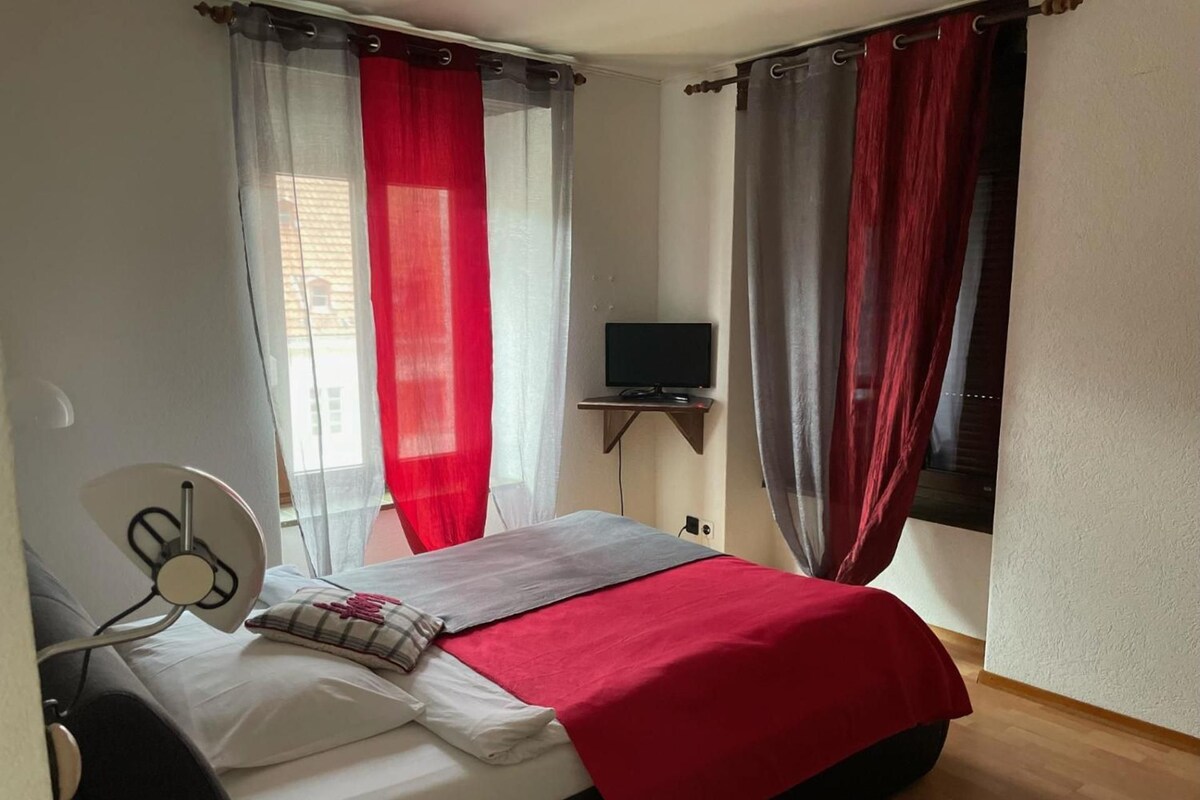 A bedroom with a bed, a TV on a stand, and curtains.