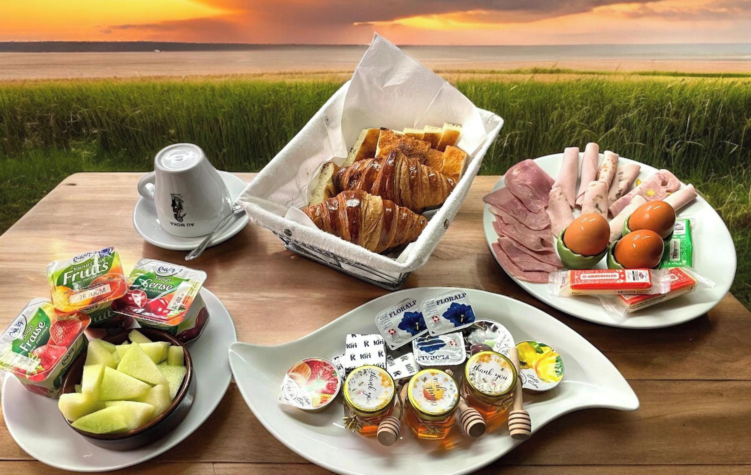A picnic setup with food and drinks on a wooden table with a view of a sunset over a field.