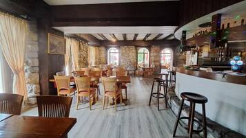 A restaurant with wooden tables and chairs, stone walls, and a bar area.