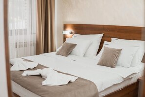 Una cama bien hecha con ropa de cama blanca y color crema, un cabecero de madera y una lámpara de noche.