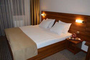 Habitación de hotel con cama de madera, ropa de cama blanca, una mesita de noche con una bandeja de comida y una ventana con cortinas.