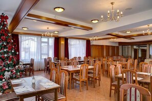Un comedor con varias mesas y sillas, un árbol de Navidad y candelabros.