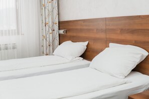 Cama doble con ropa de cama blanca en una habitación con cabecera de madera y ventana con cortinas traslúcidas.