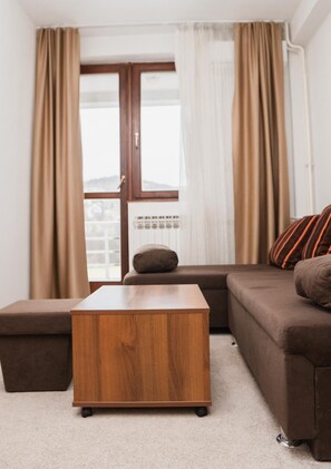 A modern living room with a sofa, a wooden coffee table, and a window with curtains. - Hotel Damis (East Sarajevo)