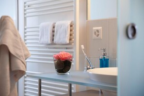 Une salle de bain avec un plan de toilette en verre, un lavabo, un porte-brosse à dents et un porte-serviettes.