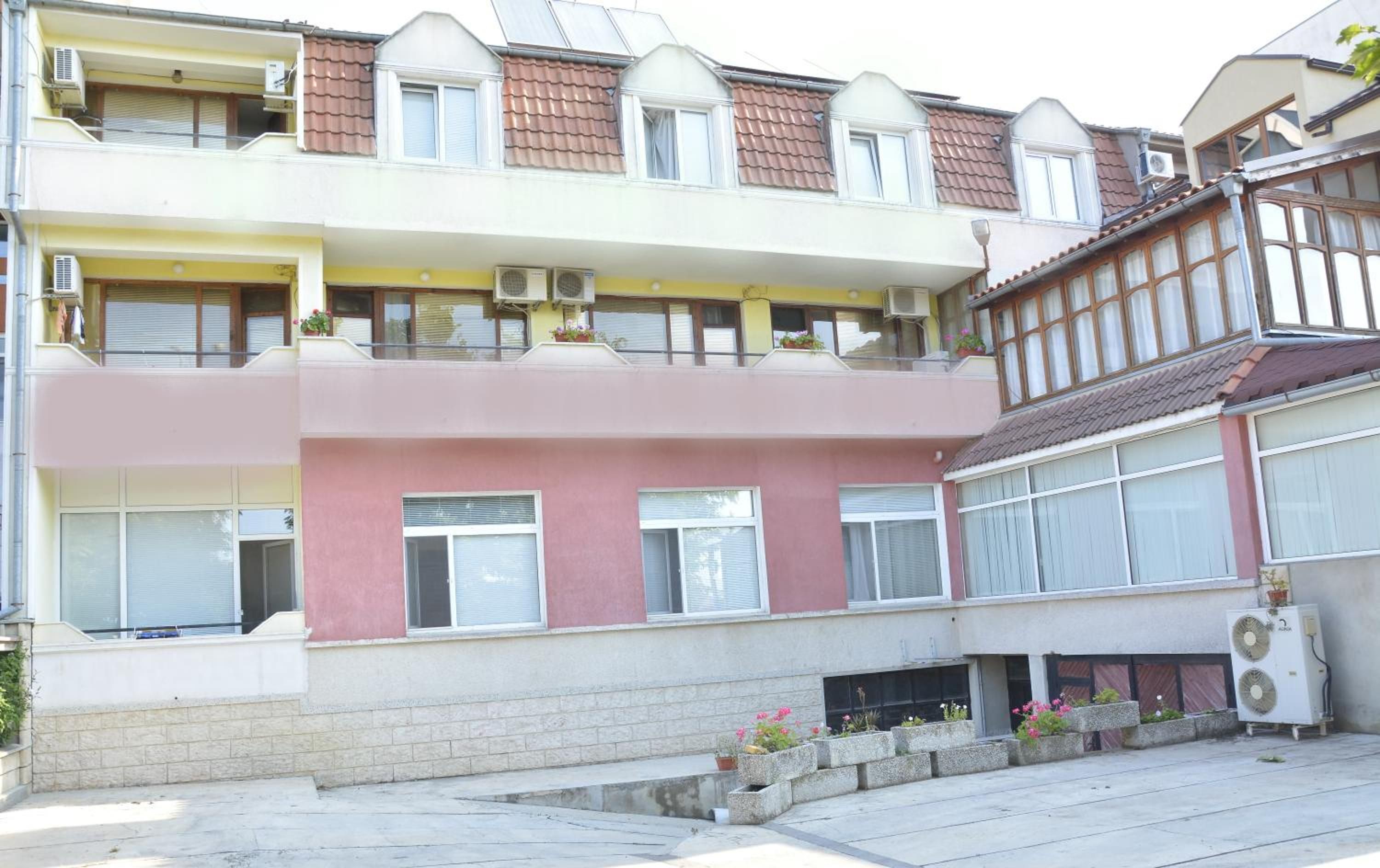 A multi-story residential building with balconies, air conditioning units, and a small garden area with potted plants.
