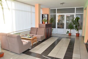 A living room with a sofa, armchair, and a coffee table. There are potted plants and a fireplace. - Hotel Wesso (Kavarna)