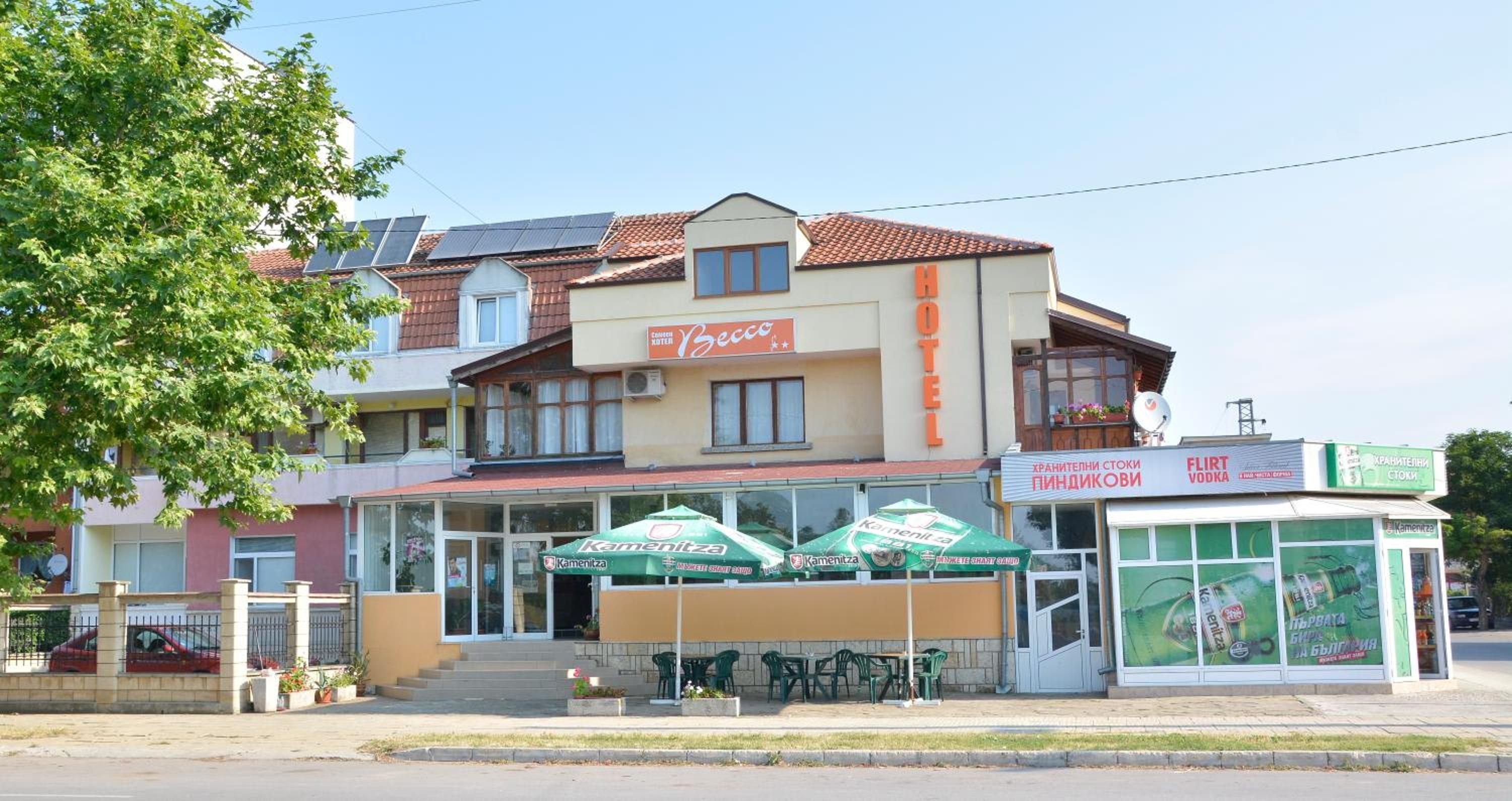 A hotel with a signboard, outdoor seating area, and a storefront with advertisements.