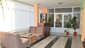 Una sala de estar con sofá, sillón y una mesa de centro. Hay plantas en macetas y una chimenea.