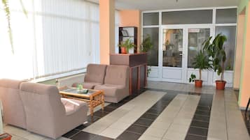 A living room with a sofa, armchair, and a coffee table. There are potted plants and a fireplace.