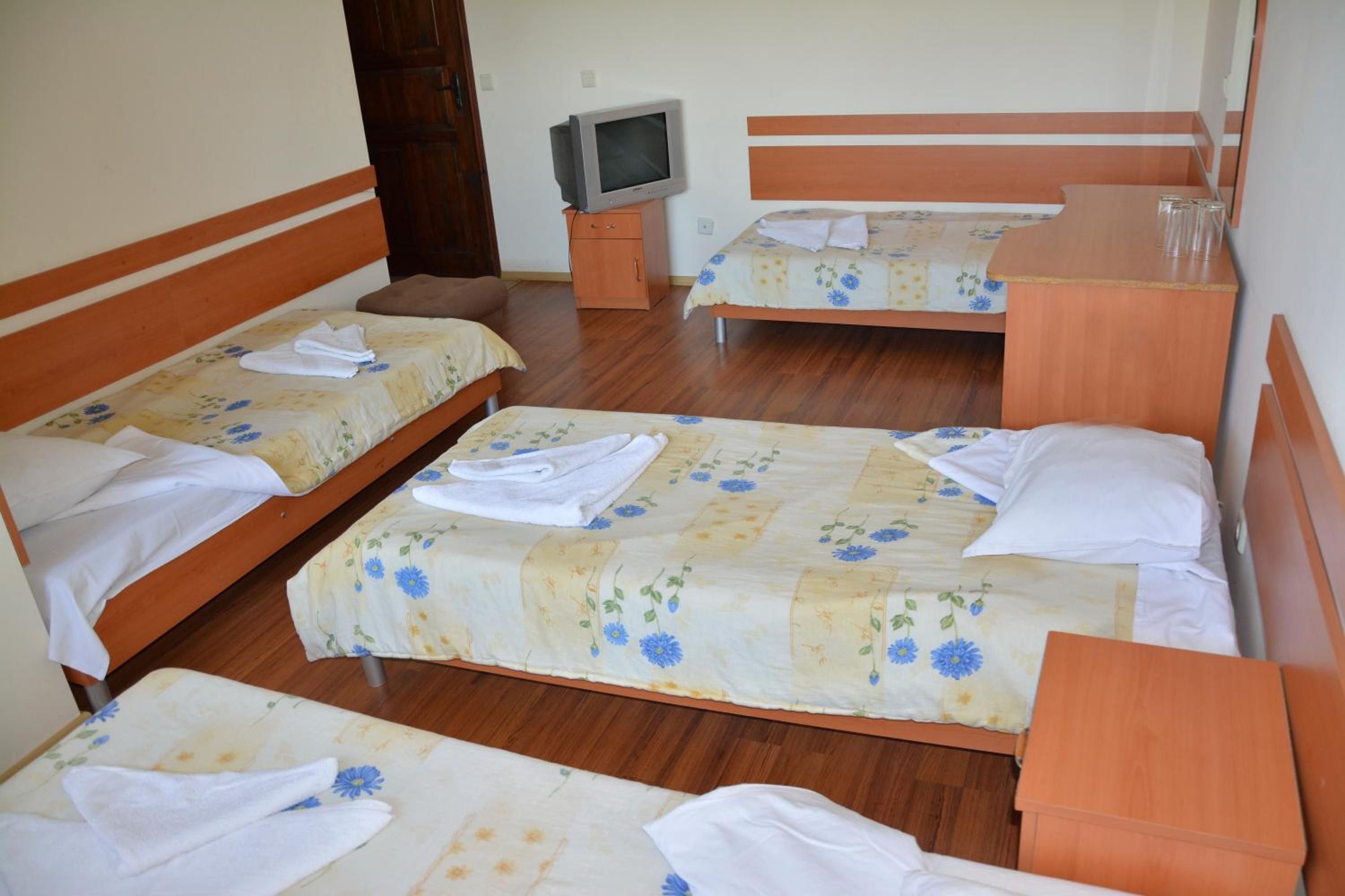A hotel room with four single beds, each with a floral bedspread and white towels. There is a wooden nightstand with a television between the beds.