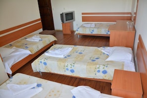 Habitación de hotel con cuatro camas individuales, cada una con cubrecama floral y toallas blancas. Hay una mesita de noche de madera con un televisor entre las camas.