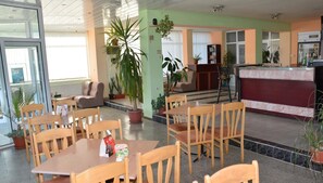 A hotel lobby with a reception desk, seating area, and potted plants. - Hotel Wesso (Kavarna)