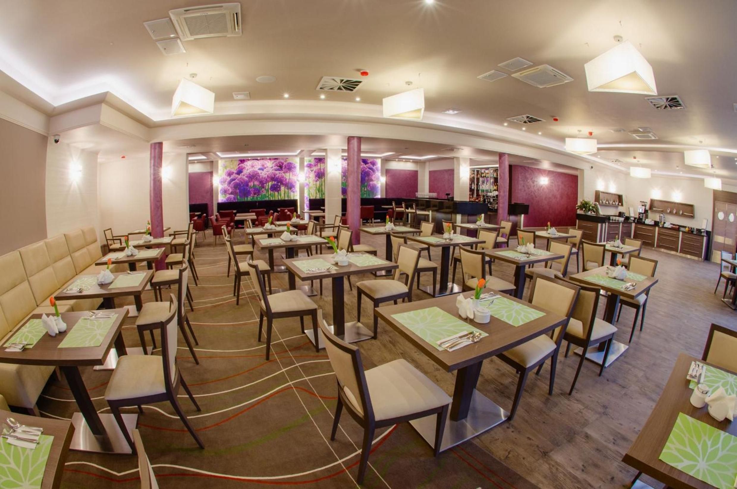 A restaurant with multiple dining tables and chairs, a bar area, and a large screen displaying floral patterns.