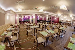 A restaurant with multiple dining tables and chairs, a bar area, and a large screen displaying floral patterns. - Hotel Olivia Medical Spa (Tokarnia)