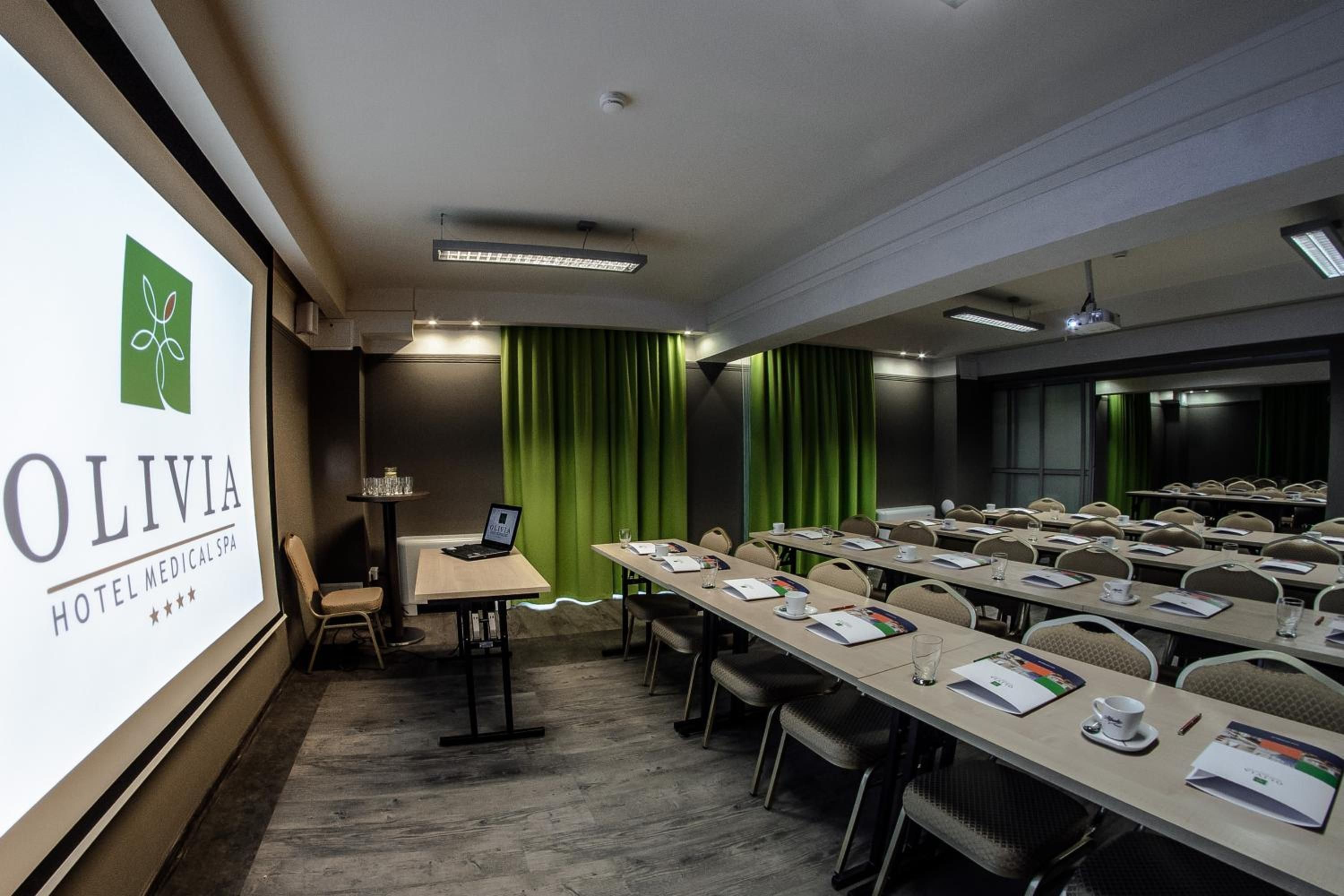 A conference room with a presentation screen, green curtains, and a laptop on a table.