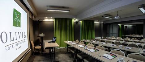 A conference room with a presentation screen, green curtains, and a laptop on a table.