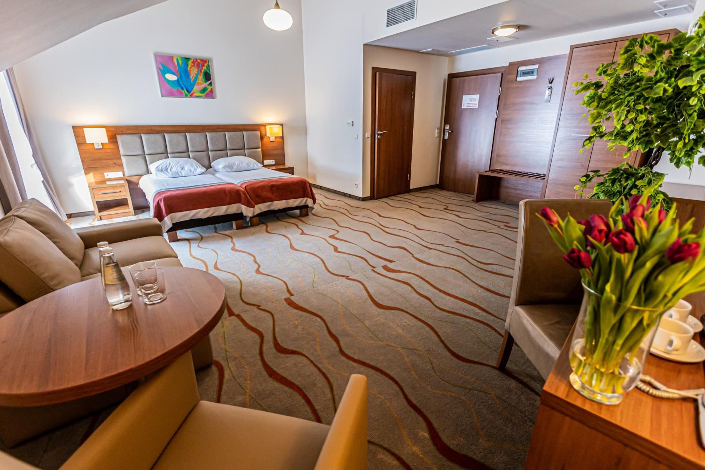 A hotel room with a bed, a sofa, a table, and a plant.
