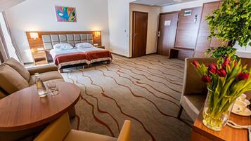 A hotel room with a bed, a sofa, a table, and a plant.