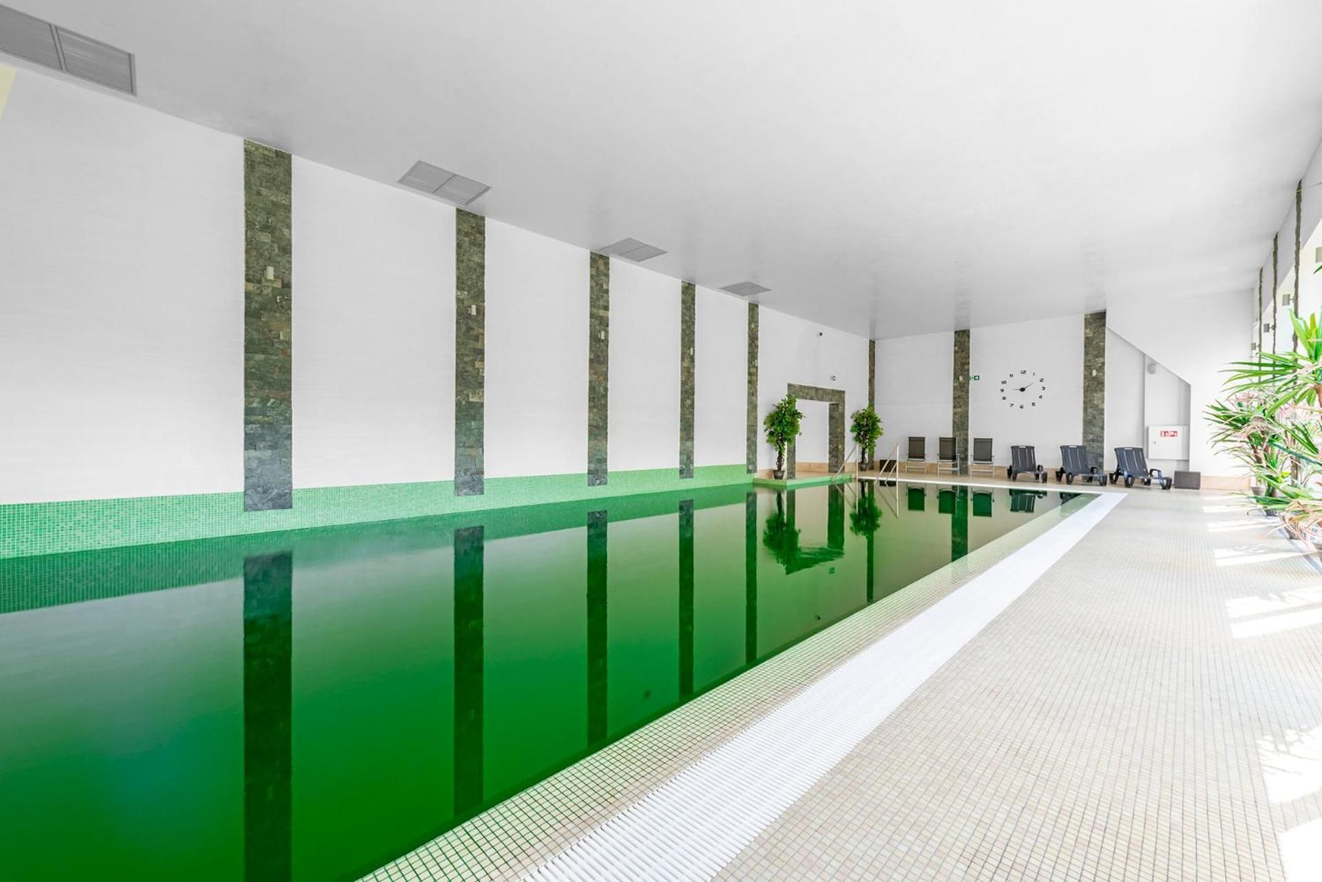 A long indoor swimming pool with a tiled floor and a greenish water surface.