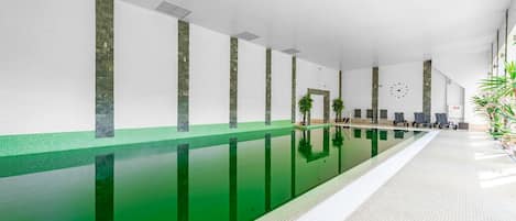 A long indoor swimming pool with a tiled floor and a greenish water surface.