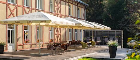 A building with a traditional half-timbered facade, outdoor seating with umbrellas, and a well-maintained garden.