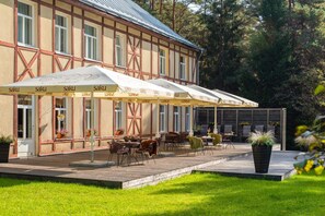 A building with a traditional half-timbered facade, outdoor seating with umbrellas, and a well-maintained garden. - Verevi Motel (Elva)