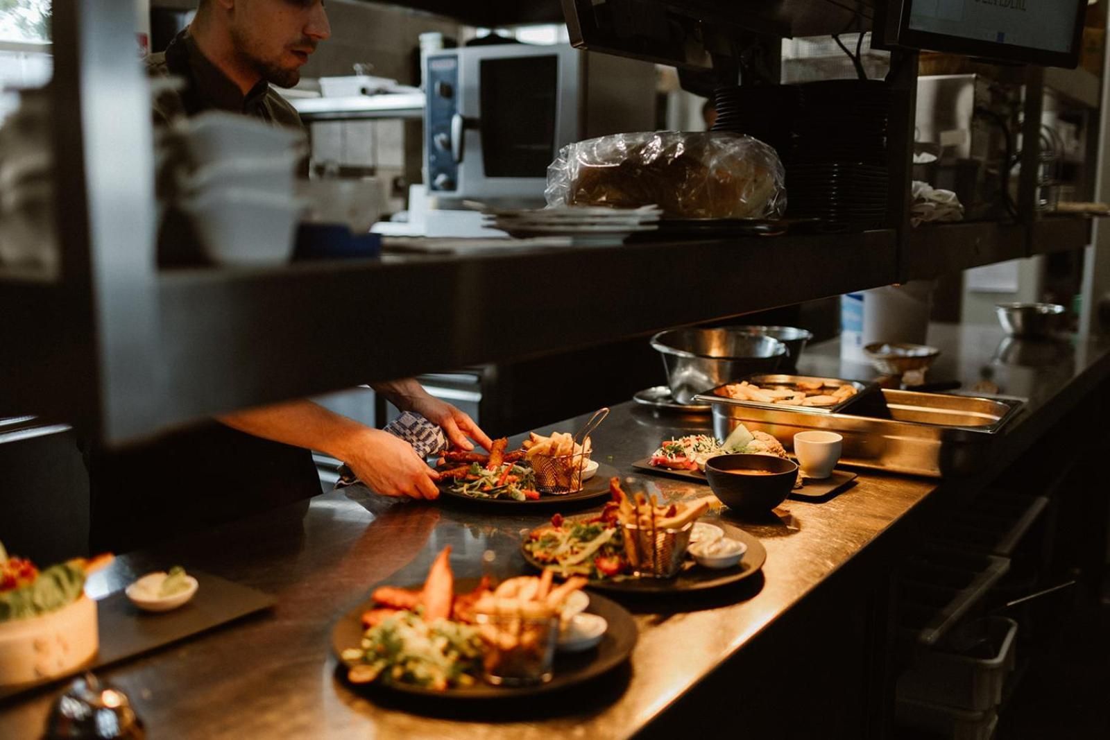 A kitchen area with a chef preparing food, various dishes on the counter, and kitchen appliances.